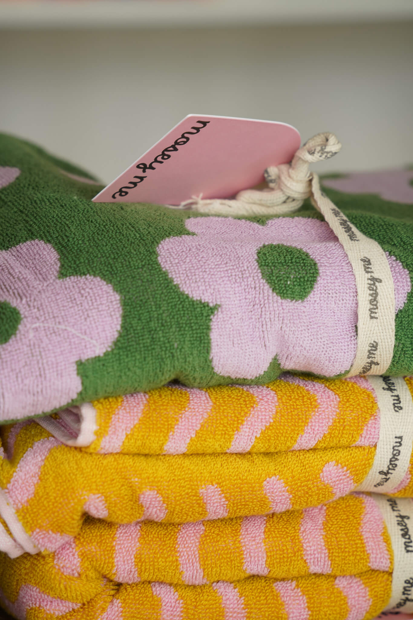 Brightly patterned towels by Mosey Me, featuring pink floral and yellow striped designs, neatly tied with branded cotton ribbons.